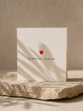 Card with a red heart and text on a stone surface with a beige background